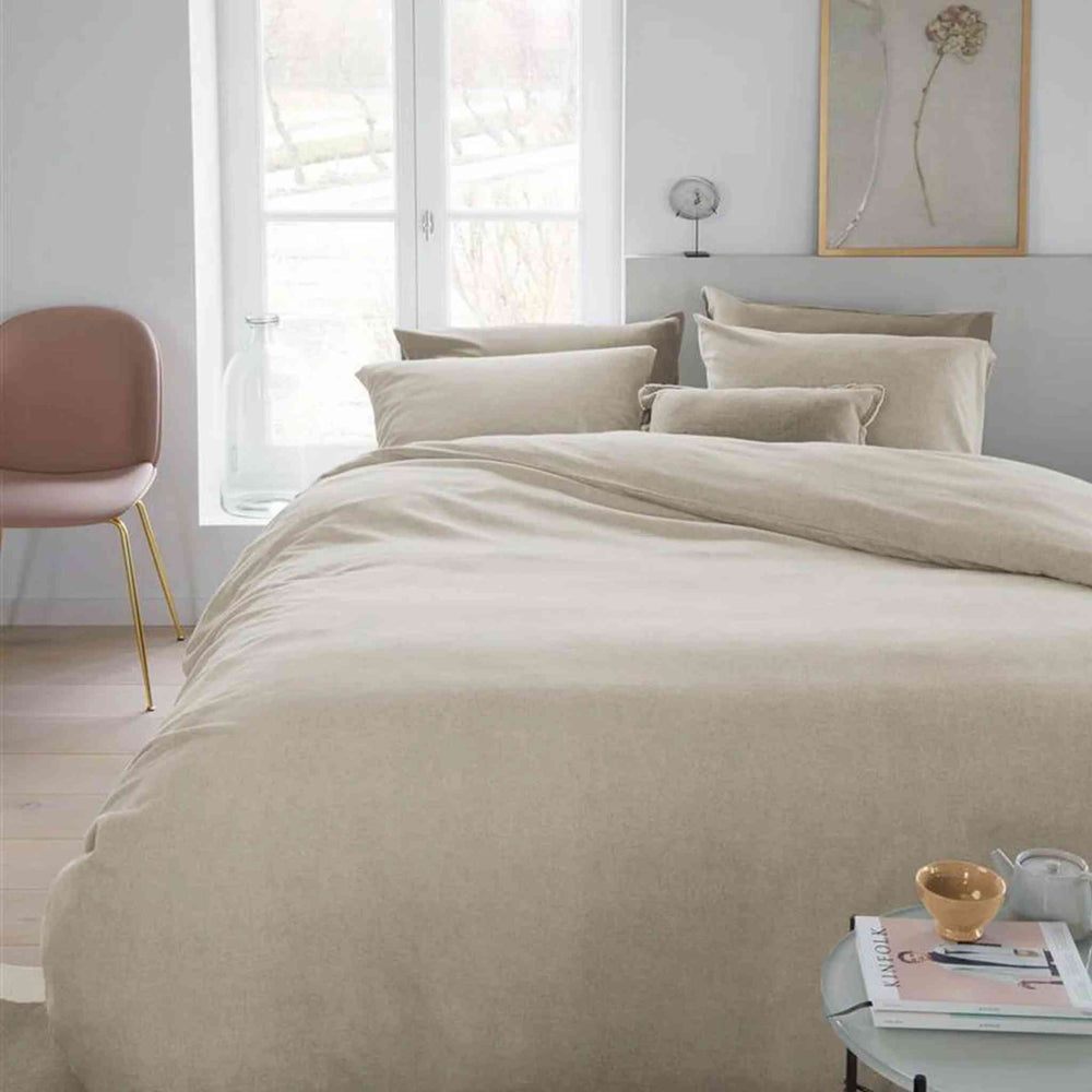 Beige bedding set on a bed in a modern bedroom with a window and decor.